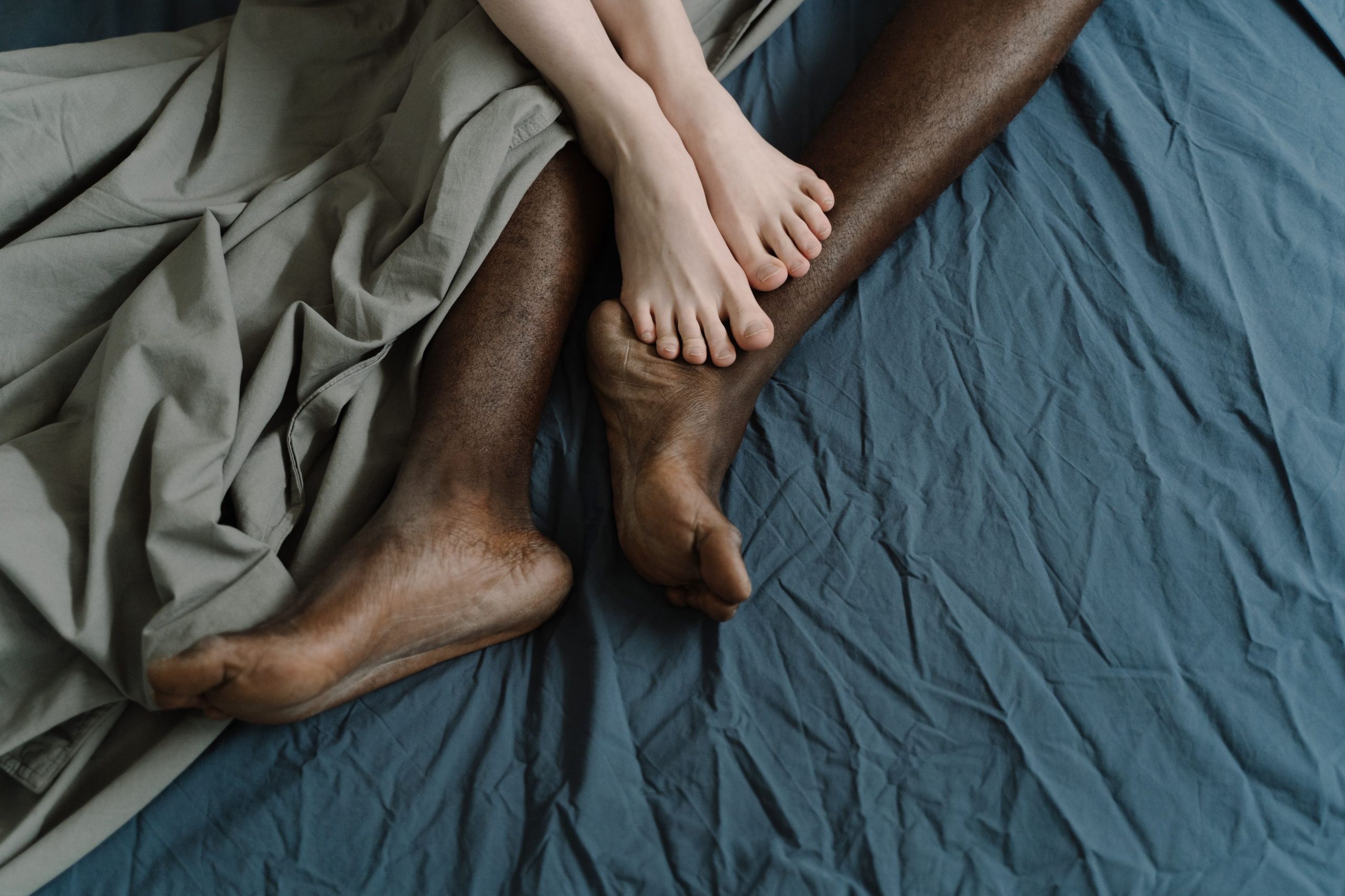 Pieds nus de couple entrelacés sur draps froissés